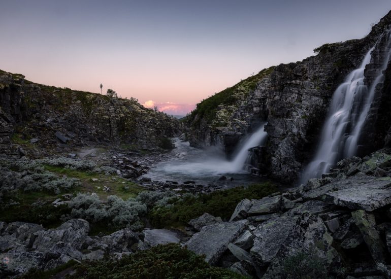 Zwei Wasserfälle stürzen nebeneinander über eine dunkle Felskante in ein felsiges Becken.