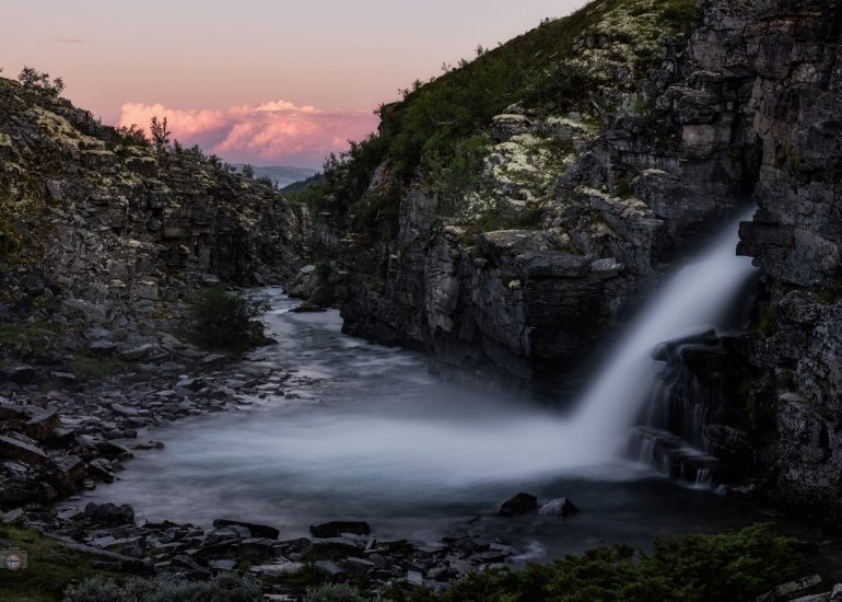 Zwei Wasserfälle stürzen nebeneinander über eine dunkle Felskante in ein felsiges Becken.