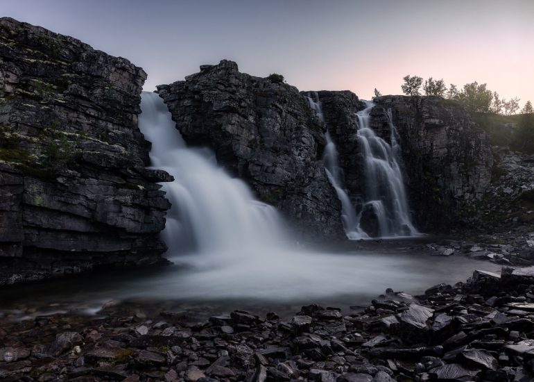 Kräftiger Wasserfall, der zwischen massiven dunklen Felswänden in ein felsiges Becken stürzt.