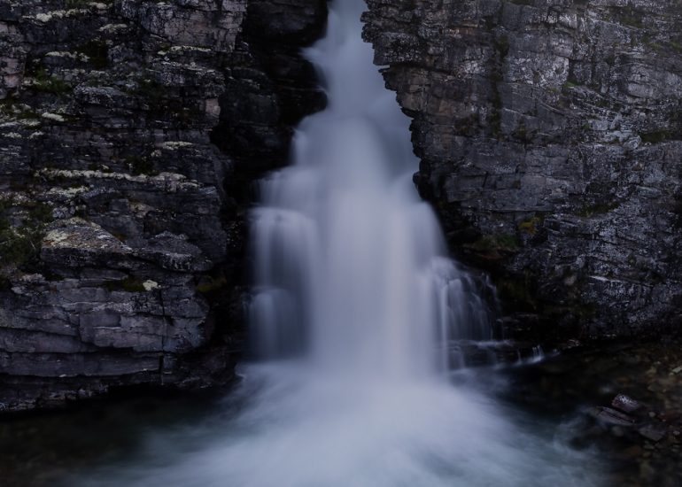 Zwei Wasserfälle stürzen nebeneinander über eine dunkle Felskante in ein felsiges Becken.