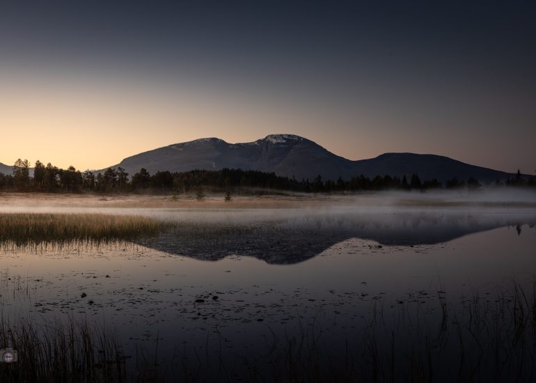 Stillen See im Morgennebel mit Spiegelung der Berge, erstes Licht des Herbstes in Norwegen, ruhige und mystische Stimmung.