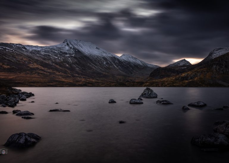 Bergsee im frühen Vormittagslicht zwischen Herbst und Winter. Sanftes Licht über den Bergen, milde Atmosphäre und stille Landschaft in Norwegen.