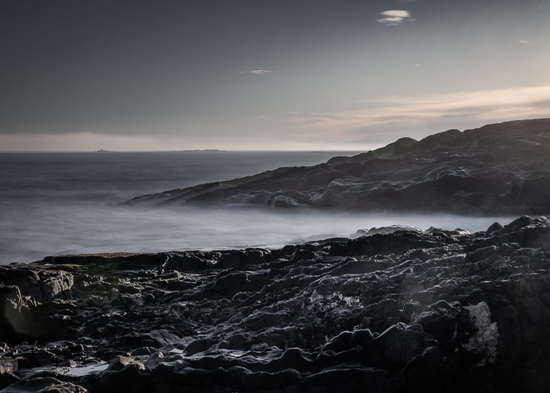Steine im Meer bei Sonnenaufgang. Weiches Winterlicht und geglättetes Wasser durch Langzeitbelichtung erzeugen eine ruhige, reduzierte Stimmung zwischen Bewegung und Stille.