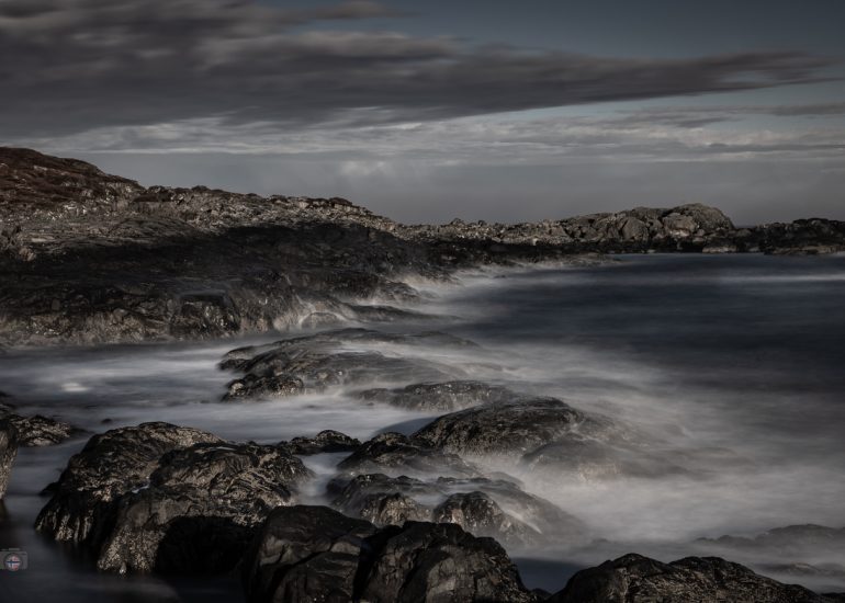 Steine im Meer bei Sonnenaufgang. Weiches Winterlicht und geglättetes Wasser durch Langzeitbelichtung erzeugen eine ruhige, reduzierte Stimmung zwischen Bewegung und Stille.