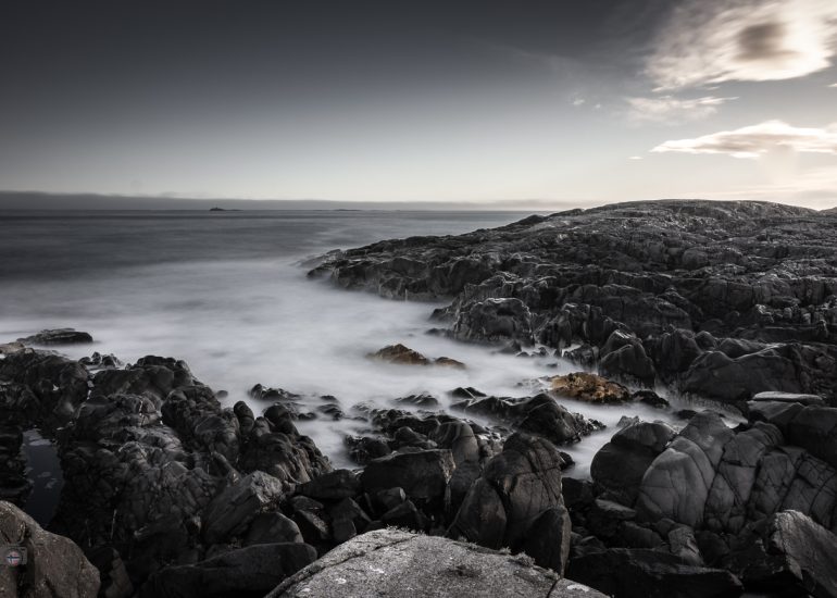 Steine im Meer bei Sonnenaufgang. Weiches Winterlicht und geglättetes Wasser durch Langzeitbelichtung erzeugen eine ruhige, reduzierte Stimmung zwischen Bewegung und Stille.