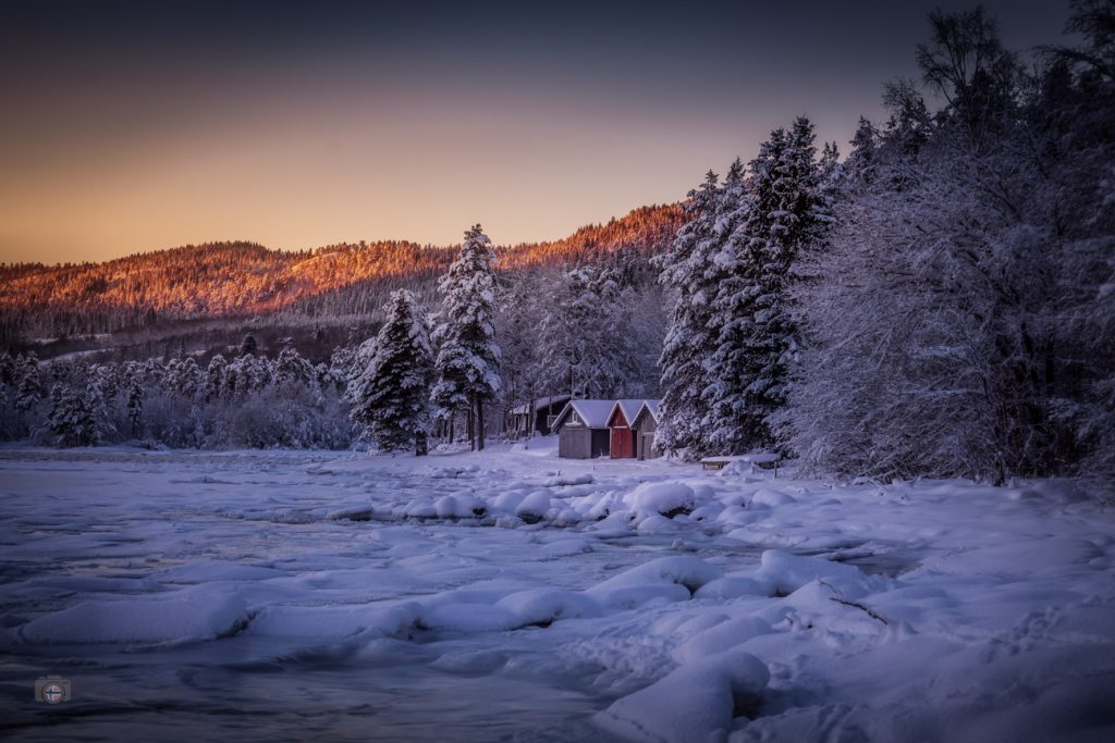 Gefrorenes Ende eines Fjords im Winterlicht. Vereiste Wasserfläche, stille Bootshäuser und ruhige Winterlandschaft bei klarem Licht.