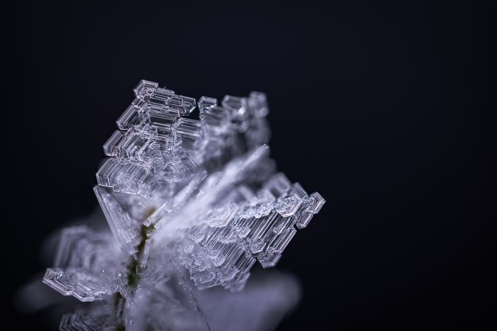 Makrofotografie von gewachsenen Eiskristallen im Winterwald. Feine, kantige Eisstrukturen vor schwarzem Hintergrund, entstanden während einer langen Kälteperiode.