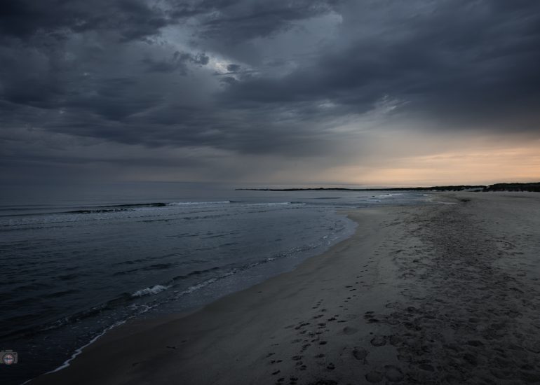 Langzeitbelichtung eines menschenleeren Strandes mit moosbewachsenen Steinen und einem großen Felsen am frühen Morgen