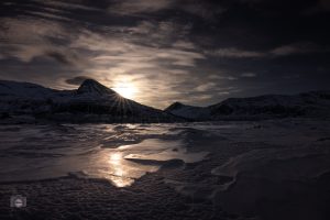 Winterberge im Morgenlicht. Gefrorener Untergrund mit Spiegelung des Sonnenaufgangs zwischen schneebedeckten Gipfeln.