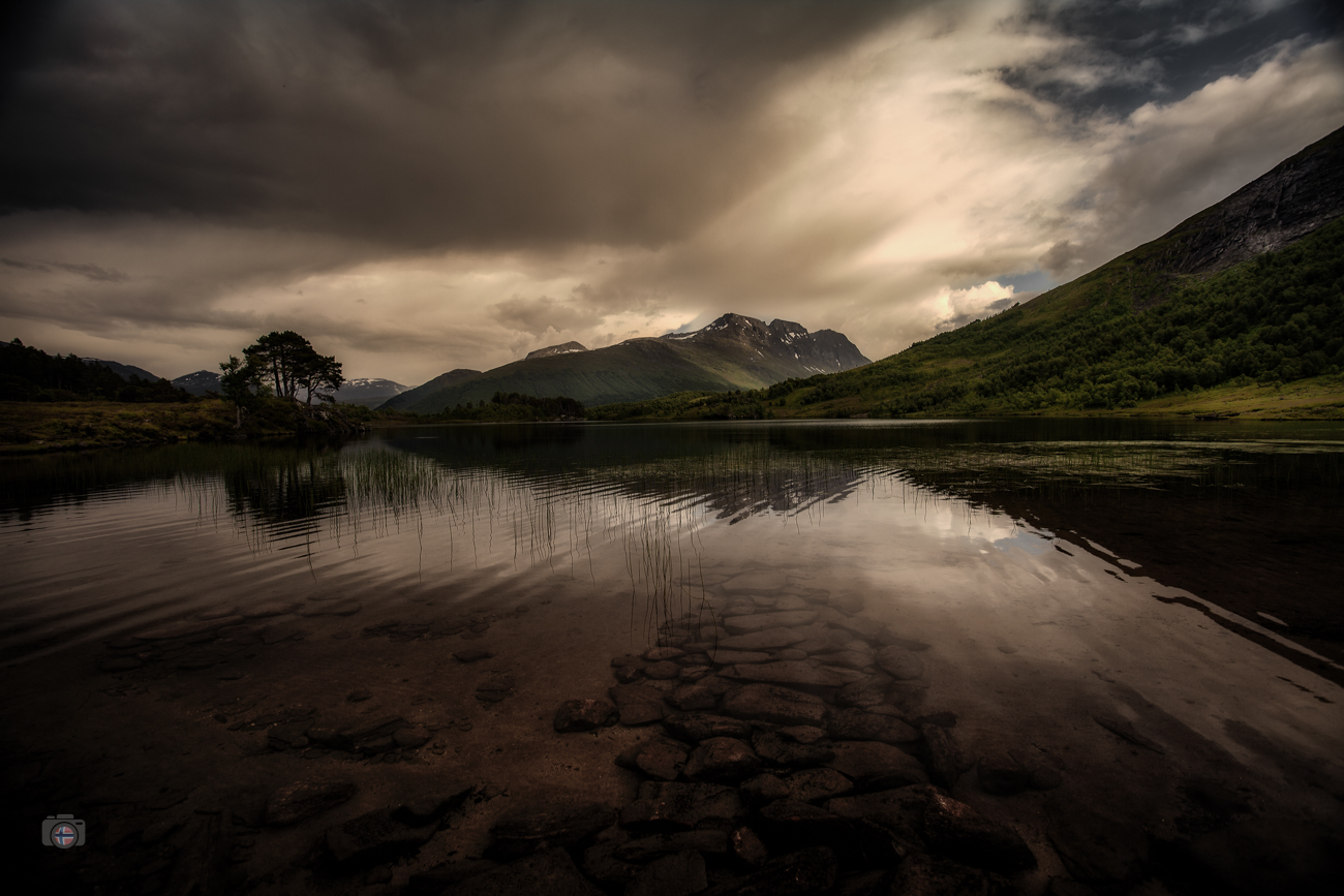 Ruhige Abendstimmung über einem Fjord mit Bergen und Spiegelung im Wasser während einer hellen nordischen Sommernacht.