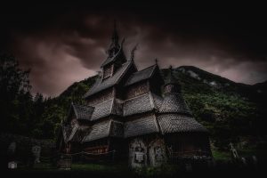 Stabkirche in Norwegen vor dunklem Himmel mit dramatischem Licht und Bergen im Hintergrund