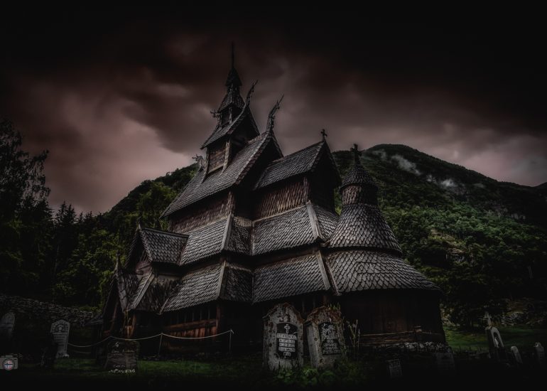 Stabkirche in Norwegen vor dunklem Himmel mit dramatischem Licht und Bergen im Hintergrund