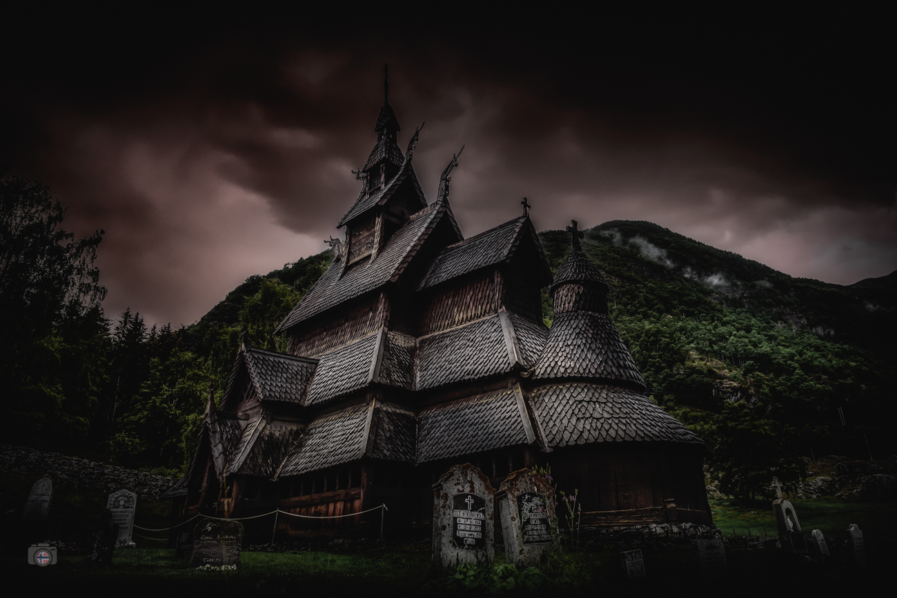 Stabkirche in Norwegen vor dunklem Himmel mit dramatischem Licht und Bergen im Hintergrund