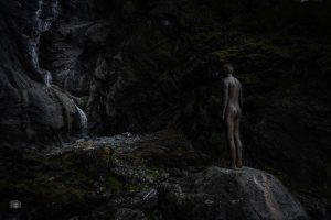 Skulptur am Felsen neben einem Wasserfall in dunkler Stimmung mit sichtbarer Wasserbewegung