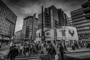 Menschen überqueren eine Straße in Oslo während der Rushhour in schwarzweiß mit moderner Architektur im Hintergrund