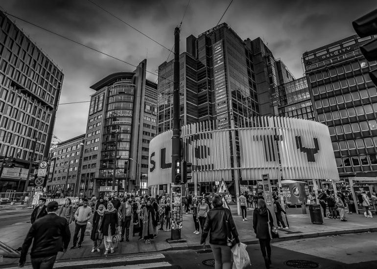 Menschen überqueren eine Straße in Oslo während der Rushhour in schwarzweiß mit moderner Architektur im Hintergrund