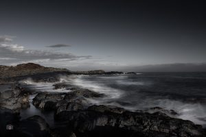 FineArt Langzeitbelichtung einer felsigen Atlantikküste mit ruhigem Wasser, dunklen Felsen und leerem Himmel.