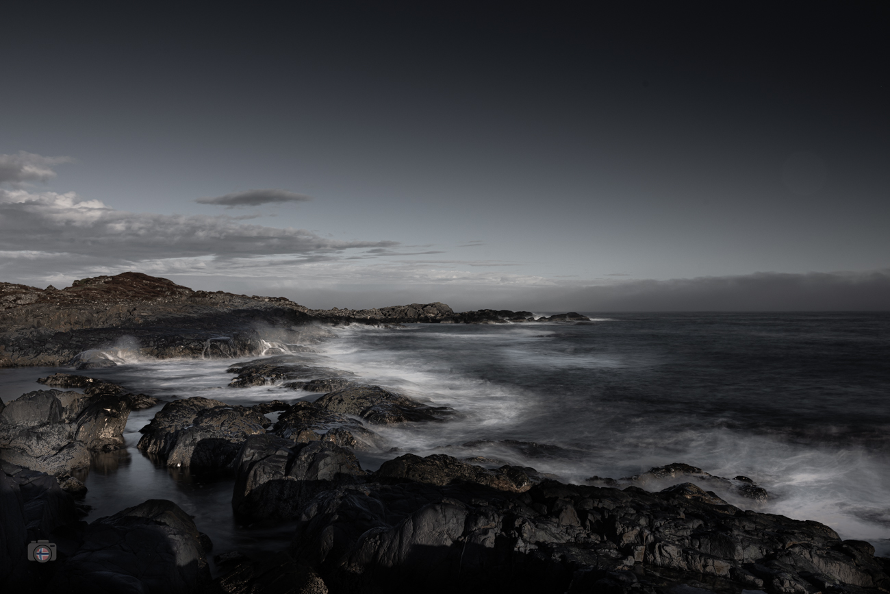 FineArt Langzeitbelichtung einer felsigen Atlantikküste mit ruhigem Wasser, dunklen Felsen und leerem Himmel.