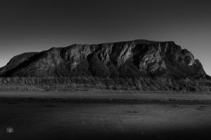 Schwarzweißes FineArt Bild eines massiven Berges vor einer offenen, ruhigen Landschaft.