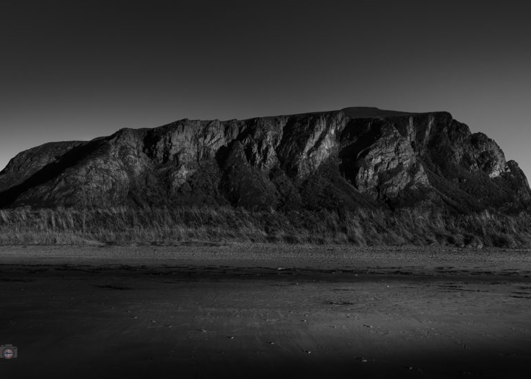 Schwarzweißes FineArt Bild eines massiven Berges vor einer offenen, ruhigen Landschaft.