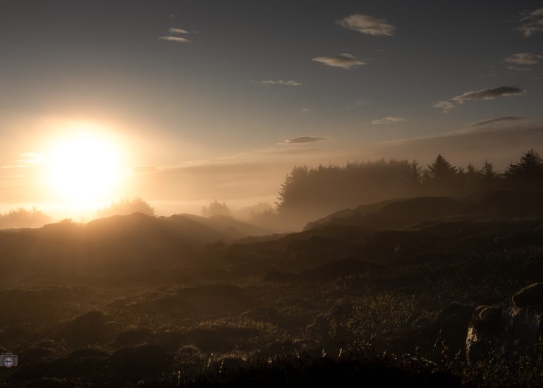 Sonnenlicht fällt über neblige Hügel am Atlantik während eines ruhigen Morgens