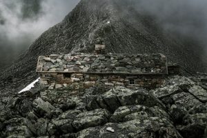 Alte Steinhütte in einer schroffen Berglandschaft mit Nebel und dunklen Wolken in Norwegen