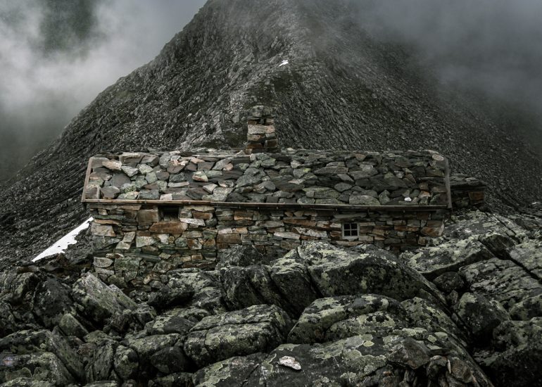 Alte Steinhütte in einer schroffen Berglandschaft mit Nebel und dunklen Wolken in Norwegen
