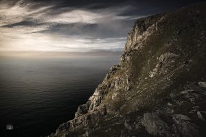 Felsküste auf den Lofoten im Licht der Mitternachtssonne mit Meer und dunklem Himmel
