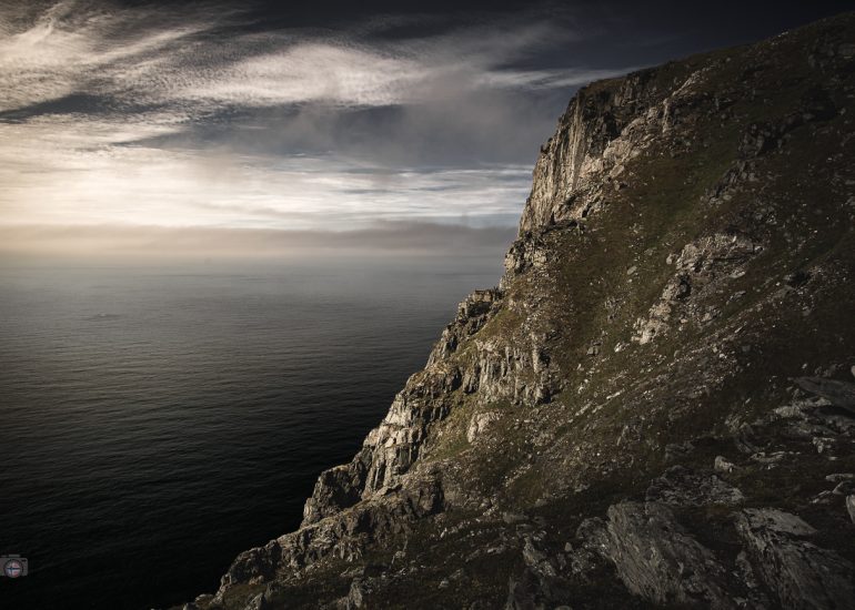 Felsküste auf den Lofoten im Licht der Mitternachtssonne mit Meer und dunklem Himmel