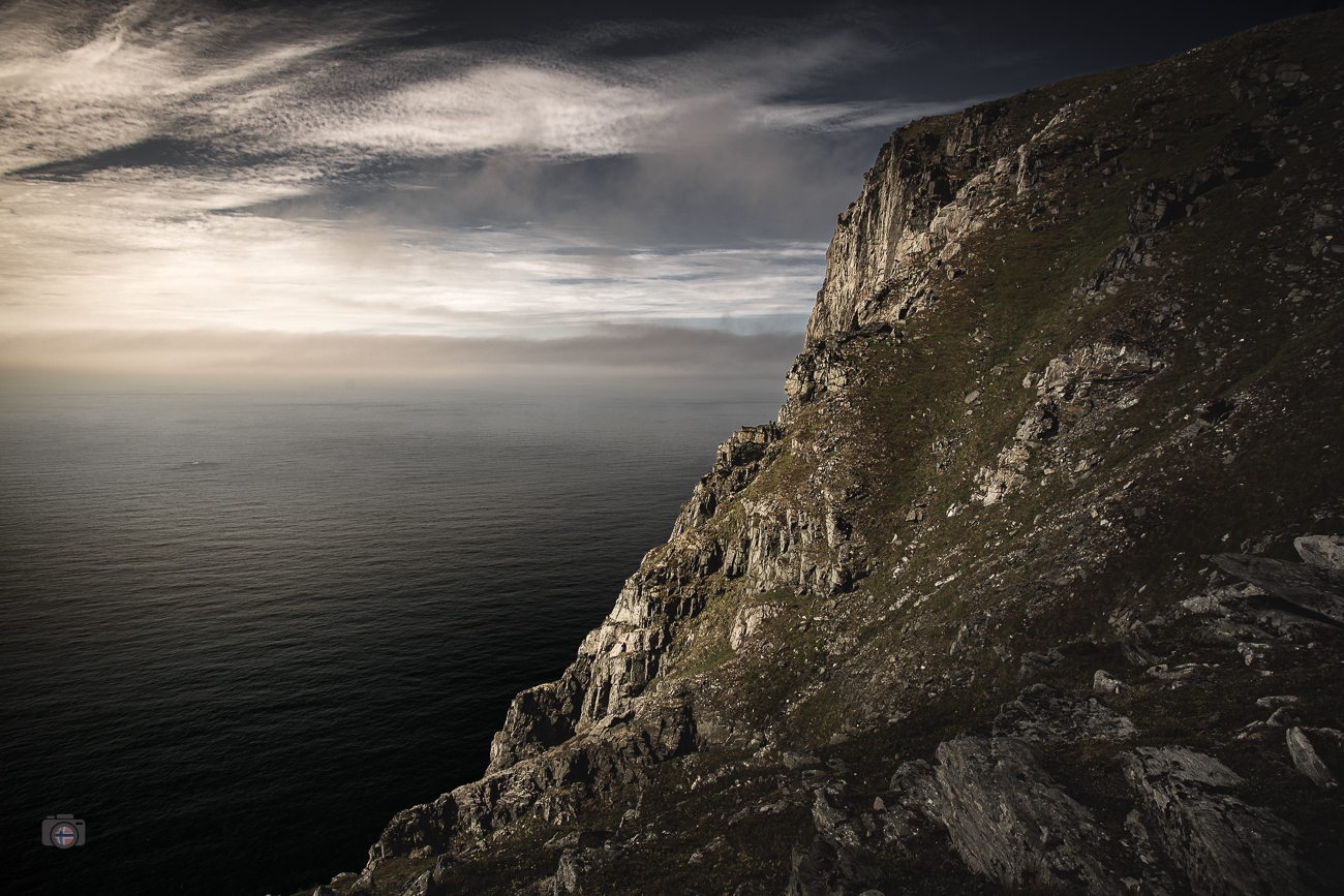 Felsküste auf den Lofoten im Licht der Mitternachtssonne mit Meer und dunklem Himmel