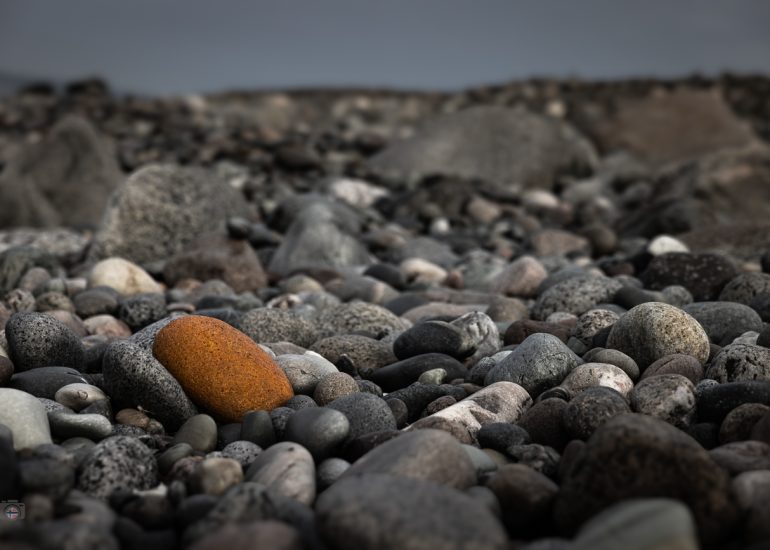 Tiefe Perspektive über unzählige runde Steine eines Küstenstrandes mit Meer und bewölktem Himmel im Hintergrund.