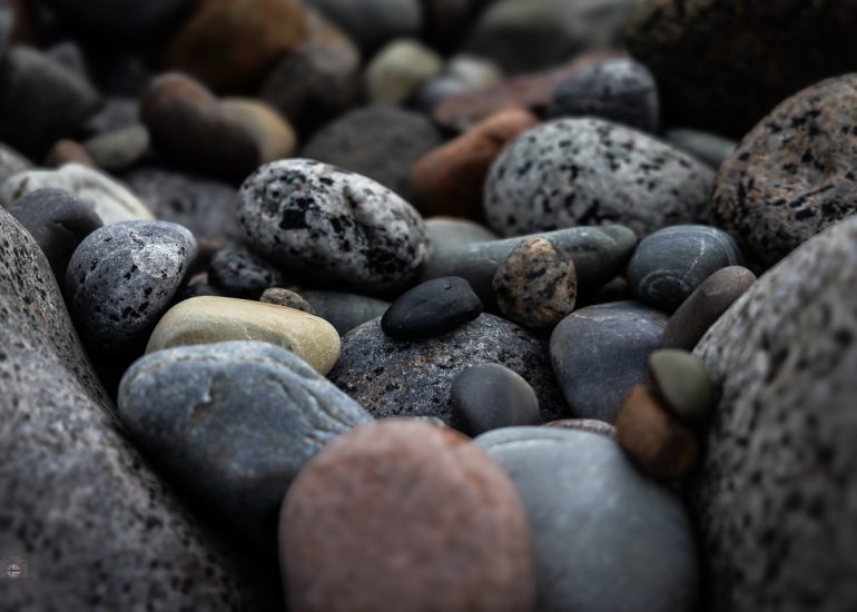 Tiefe Perspektive über unzählige runde Steine eines Küstenstrandes mit Meer und bewölktem Himmel im Hintergrund.