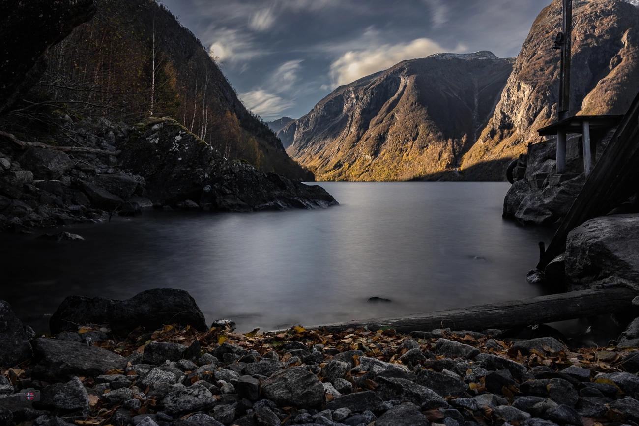 Steiniges Ufer einer geschützten Bucht an einem Bergsee mit geglättetem Wasser und herbstlichen Bergen