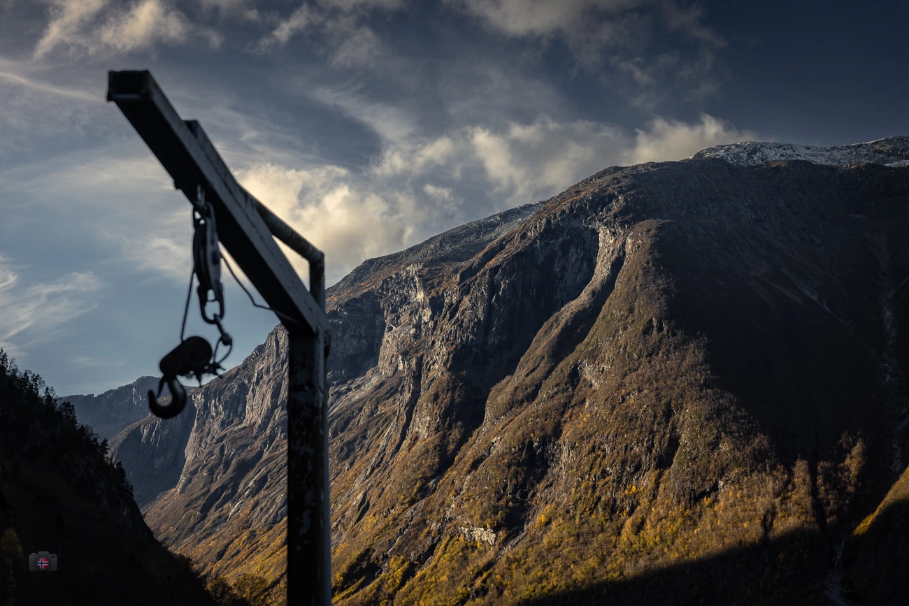 Dunkler Metallhaken im Vordergrund vor herbstlich beleuchteten Bergen an einem Bergsee