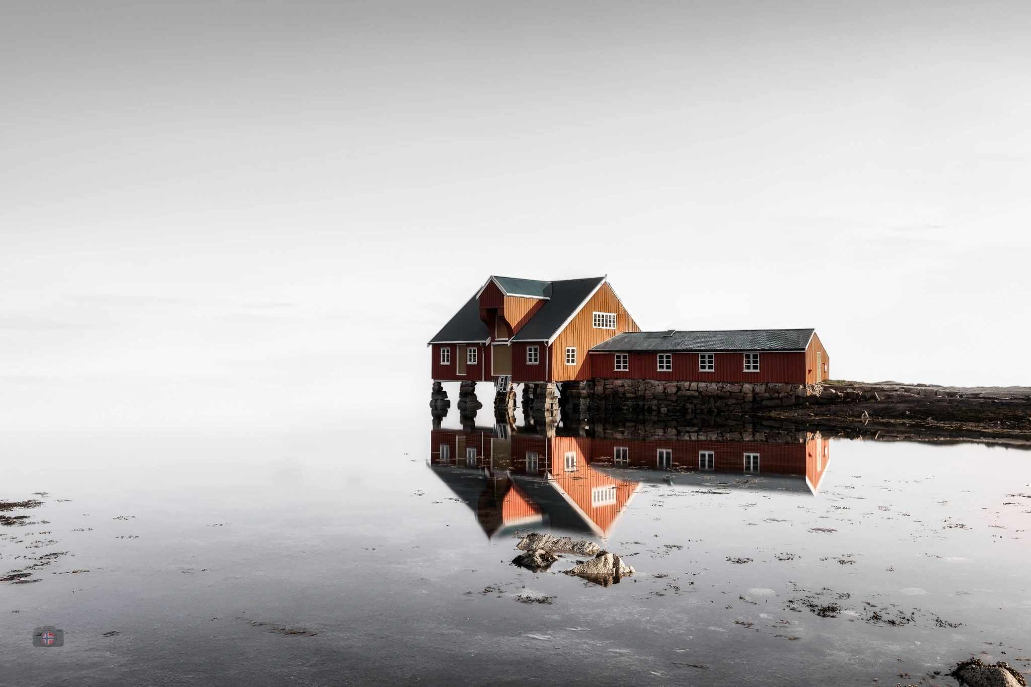 Rotes norwegisches Fischerhaus im ruhigen Wasser gespiegelt.